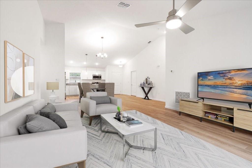A living room with light wood floors, a gray sofa, and an open-concept kitchen beyond — 192 PERSIMMON DRIVE, PALM COAST, FL