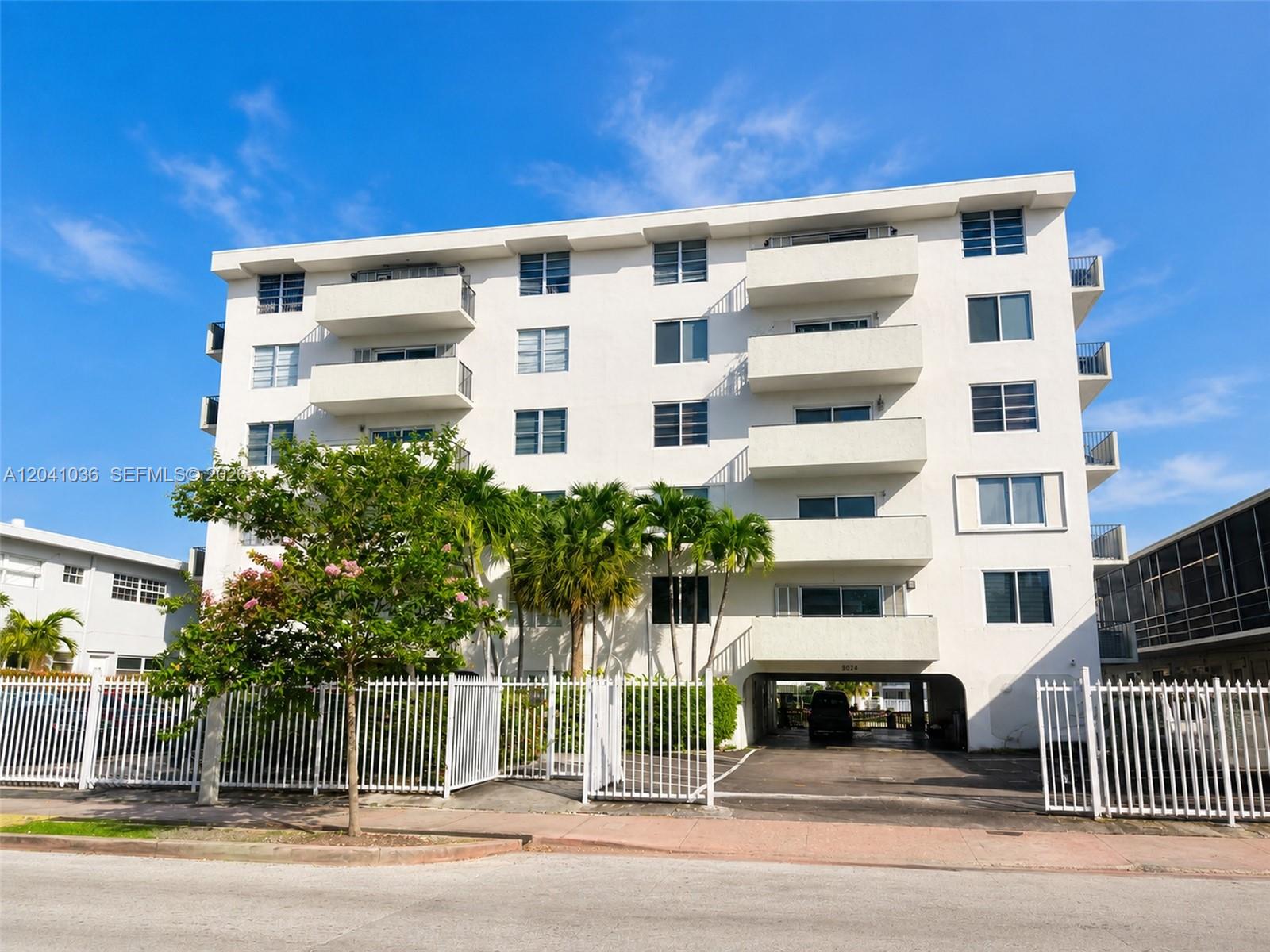 A multi-story white apartment building features balconies and a ground-level parking area — 8024 Tatum Waterway Dr # 2B, Miami Beach FL 33141, MIAMI BEACH, FL