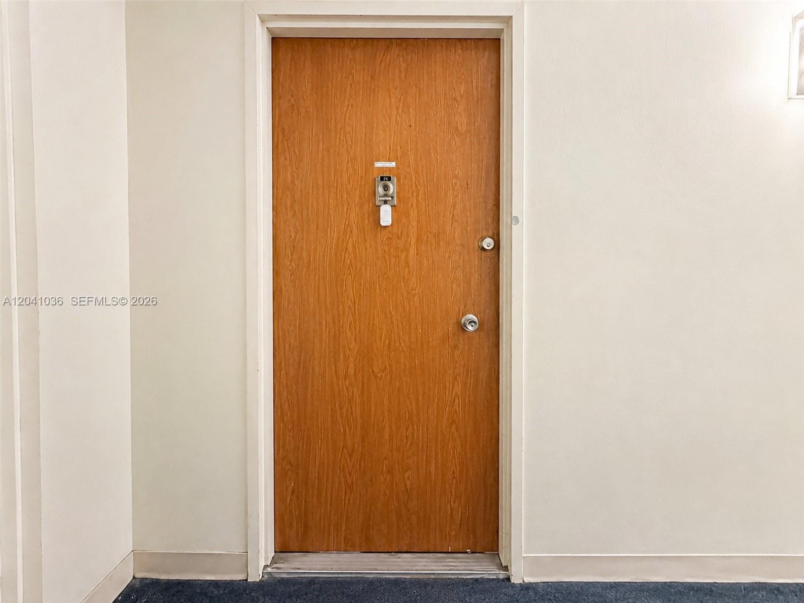 A wood-grain door with a peephole and two locks is set in a plain wall — 8024 Tatum Waterway Dr # 2B, Miami Beach FL 33141, MIAMI BEACH, FL