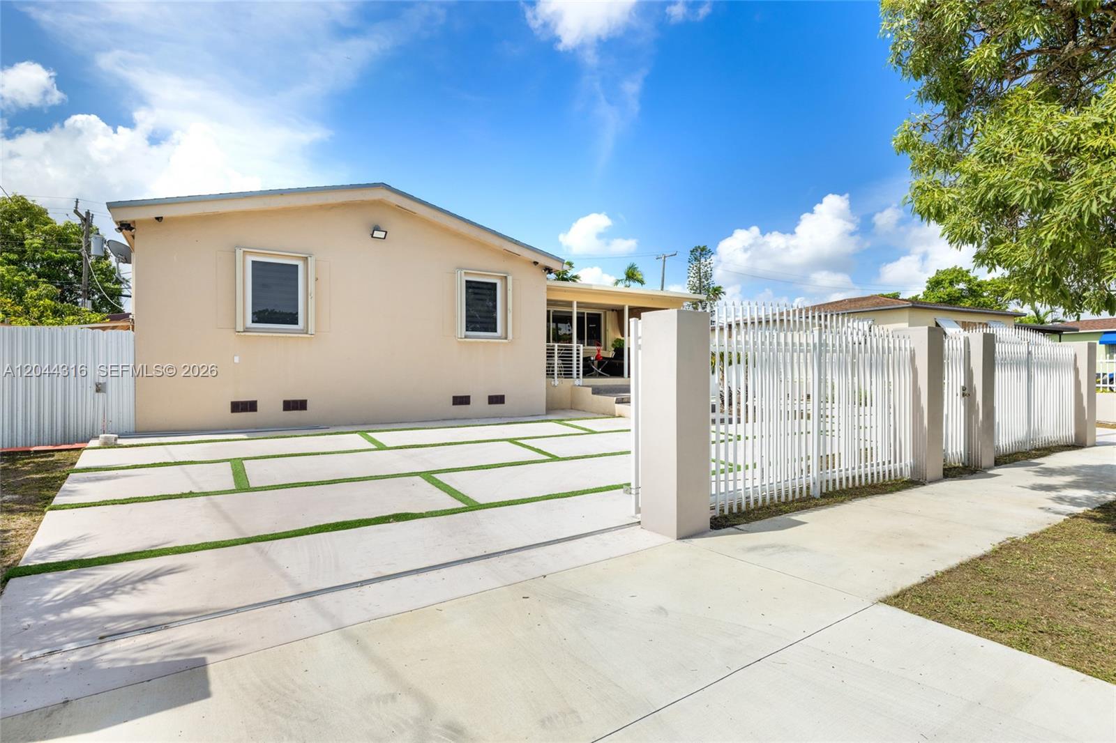 A beige house with a concrete driveway featuring grass strips and a white metal fence — 8330 SW 25th St, Miami FL 33155, MIAMI, FL