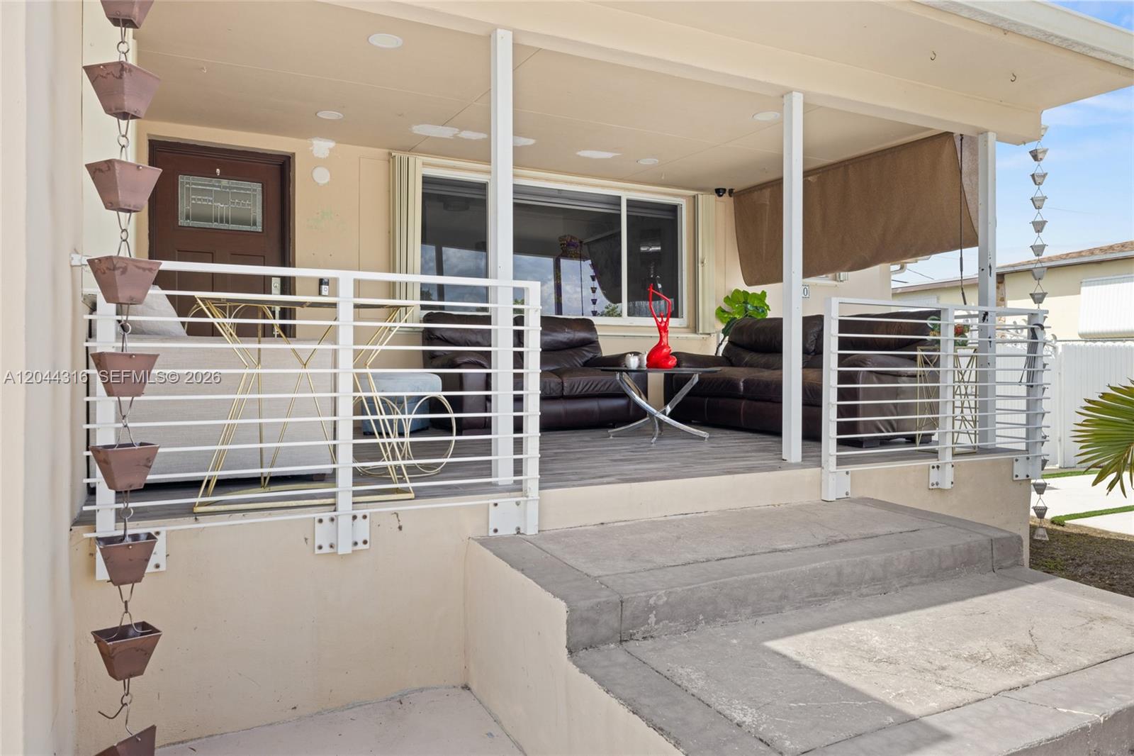 A covered porch features a white metal railing, brown leather furniture, and rain chains — 8330 SW 25th St, Miami FL 33155, MIAMI, FL