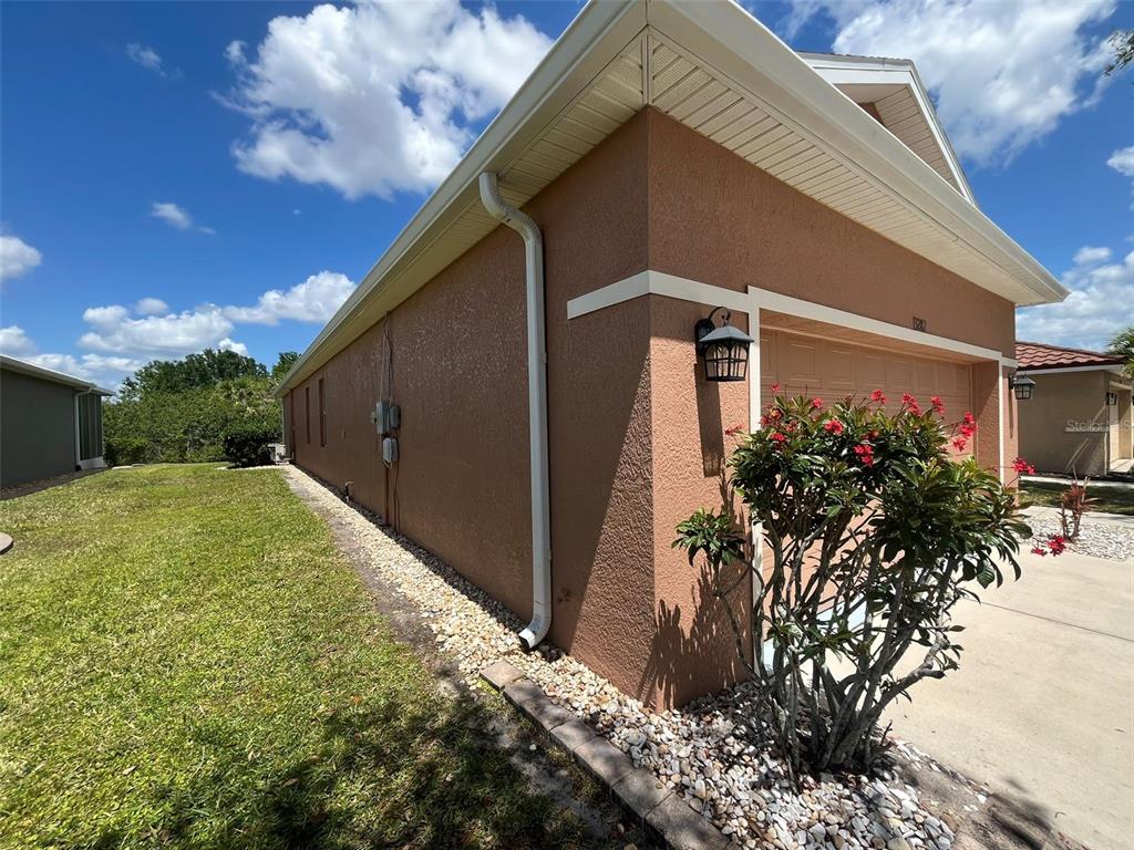 A side view of a tan stucco house with a garage and a white downspout — 13282 SW PEMBROKE CIRCLE N, LAKE SUZY, FL