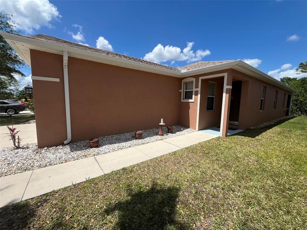 A side view of a tan stucco house with a concrete walkway and rock landscaping — 13282 SW PEMBROKE CIRCLE N, LAKE SUZY, FL