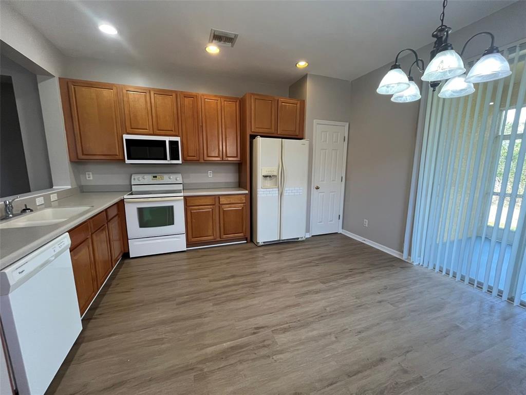 A kitchen with wood cabinets, white appliances, and wood-look flooring next to a dining area — 13282 SW PEMBROKE CIRCLE N, LAKE SUZY, FL