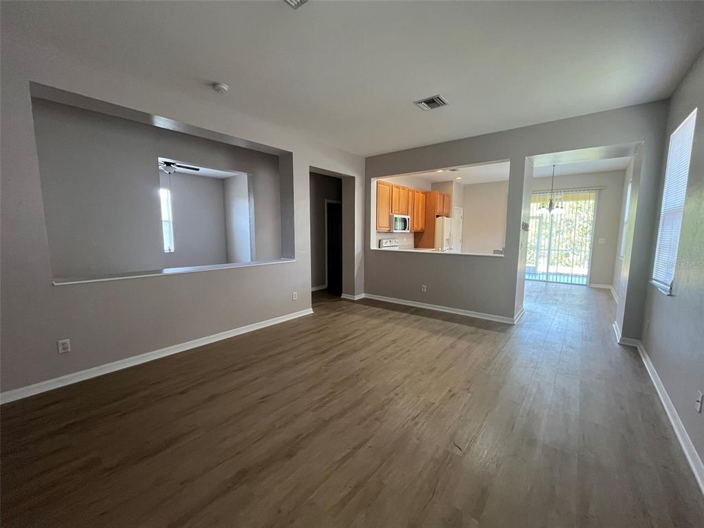 A living room with wood-look flooring, a large wall cutout, and an open kitchen view — 13282 SW PEMBROKE CIRCLE N, LAKE SUZY, FL