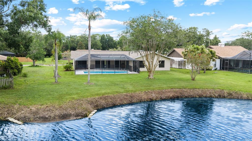 A backyard with a swimming pool, screened enclosure, and pond view behind a residential house — 14011 WOLCOTT DRIVE, TAMPA, FL