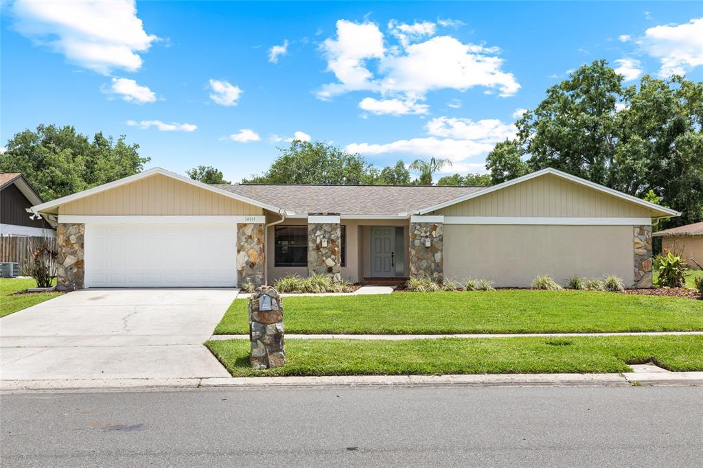 A single-story house with a white garage, stone accents, and a beige exterior — 14011 WOLCOTT DRIVE, TAMPA, FL