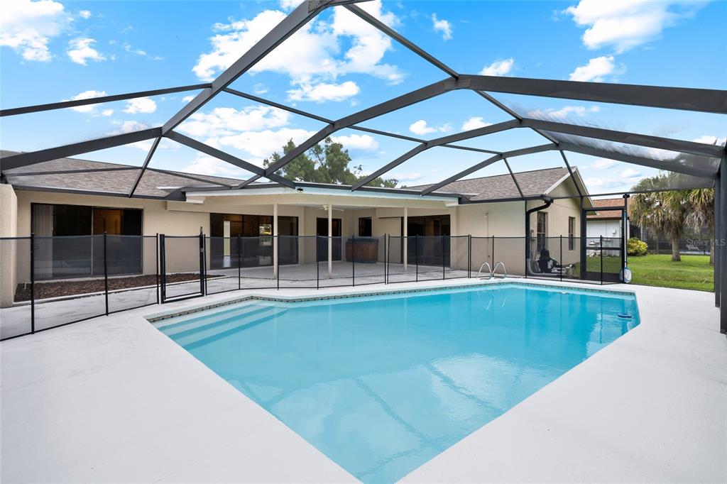 A swimming pool with a safety fence is enclosed by a screened lanai behind a house — 14011 WOLCOTT DRIVE, TAMPA, FL