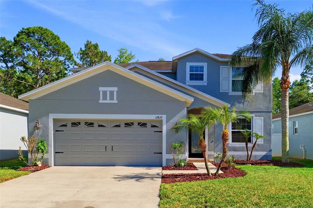 A two-story gray house with a two-car garage and a small palm tree out front — 12832 SAULSTON PLACE, HUDSON, FL