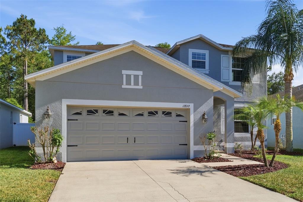 A two-story house with a gray stucco exterior, a two-car garage, and a palm tree — 12832 SAULSTON PLACE, HUDSON, FL