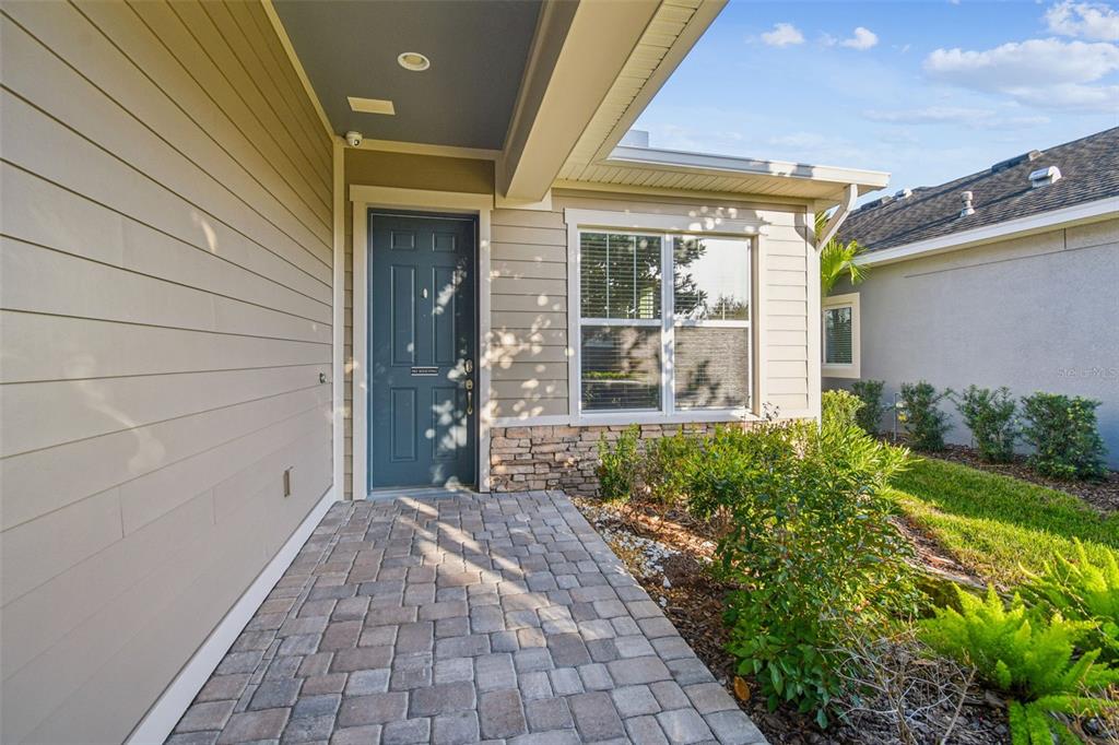 A paved walkway leads to a front door with tan siding and stone accents — 6036 PLOVER MEADOW STREET, LITHIA, FL