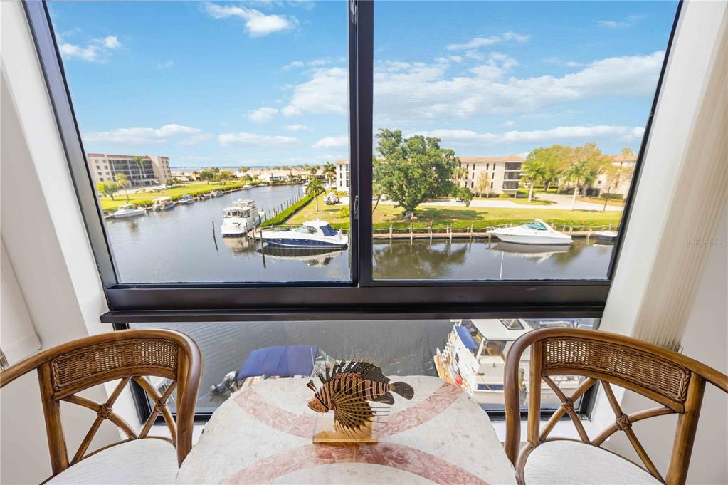 A small table with two wicker chairs overlooks a canal filled with docked boats — 25188 MARION AVENUE UNIT D308, PUNTA GORDA, FL