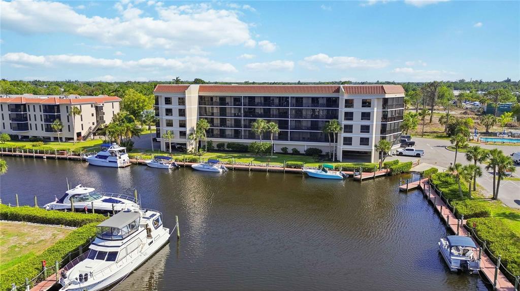 An aerial view shows a multi-story apartment building situated along a canal with docked boats — 25188 MARION AVENUE UNIT D308, PUNTA GORDA, FL