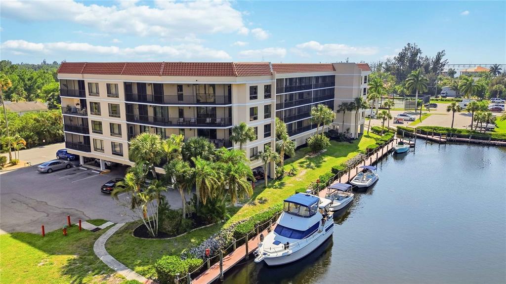 An aerial view shows a multi-story apartment building next to a canal with docked boats — 25188 MARION AVENUE UNIT D308, PUNTA GORDA, FL