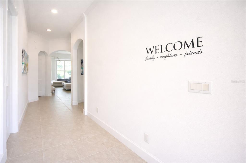 A bright hallway features light tile flooring, arched doorways, and a welcome wall decal — 4084 OAKTREE DRIVE, DAVENPORT, FL