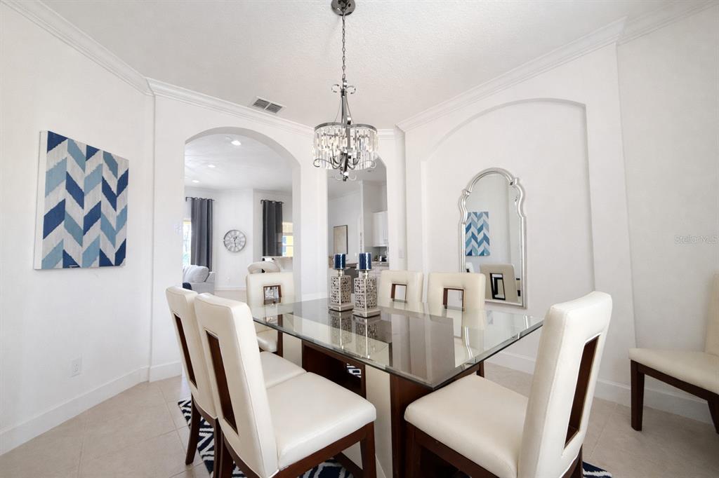 A dining room features a glass-top table, white upholstered chairs, and a crystal chandelier — 4084 OAKTREE DRIVE, DAVENPORT, FL