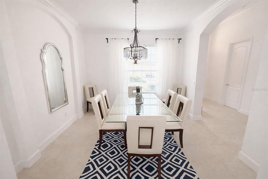 A dining room features a glass table, white upholstered chairs, a chandelier, and a patterned rug — 4084 OAKTREE DRIVE, DAVENPORT, FL