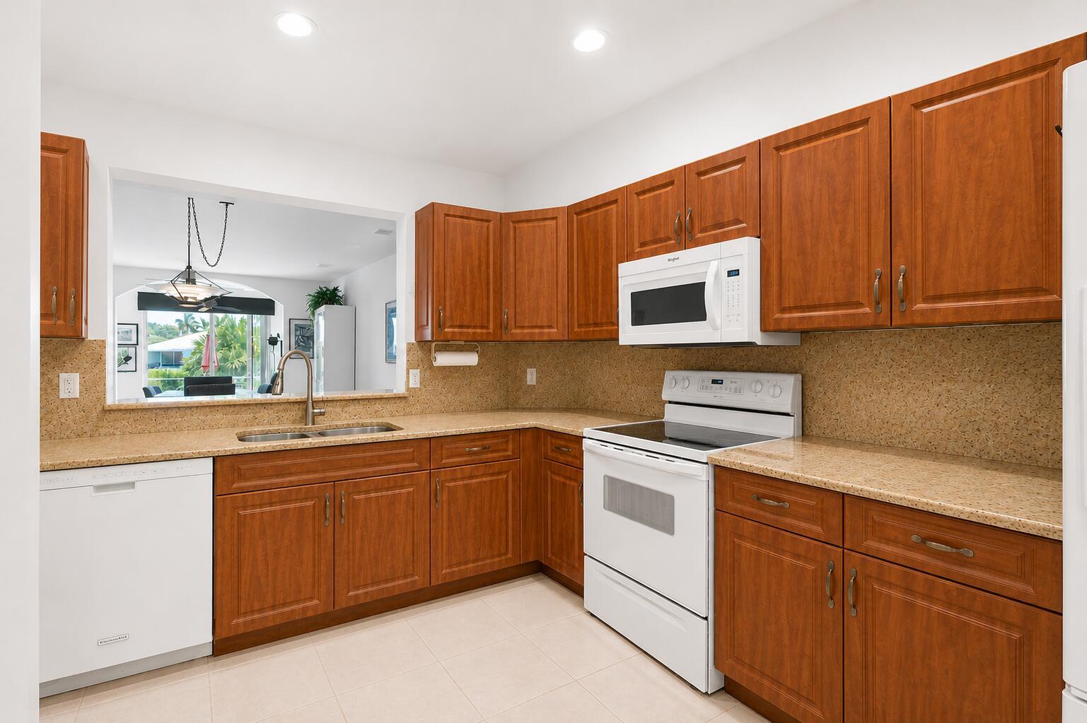 A kitchen with wood cabinets, tan countertops, white appliances, and a pass-through window to outside — 10773 Royal Caribbean Circle, Boynton Beach FL 33437, BOYNTON BEACH, FL