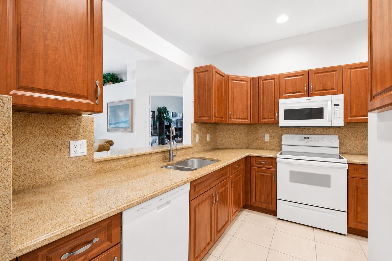 A kitchen features wood cabinets, granite countertops, white appliances, and a pass-through window — 10773 Royal Caribbean Circle, Boynton Beach FL 33437, BOYNTON BEACH, FL