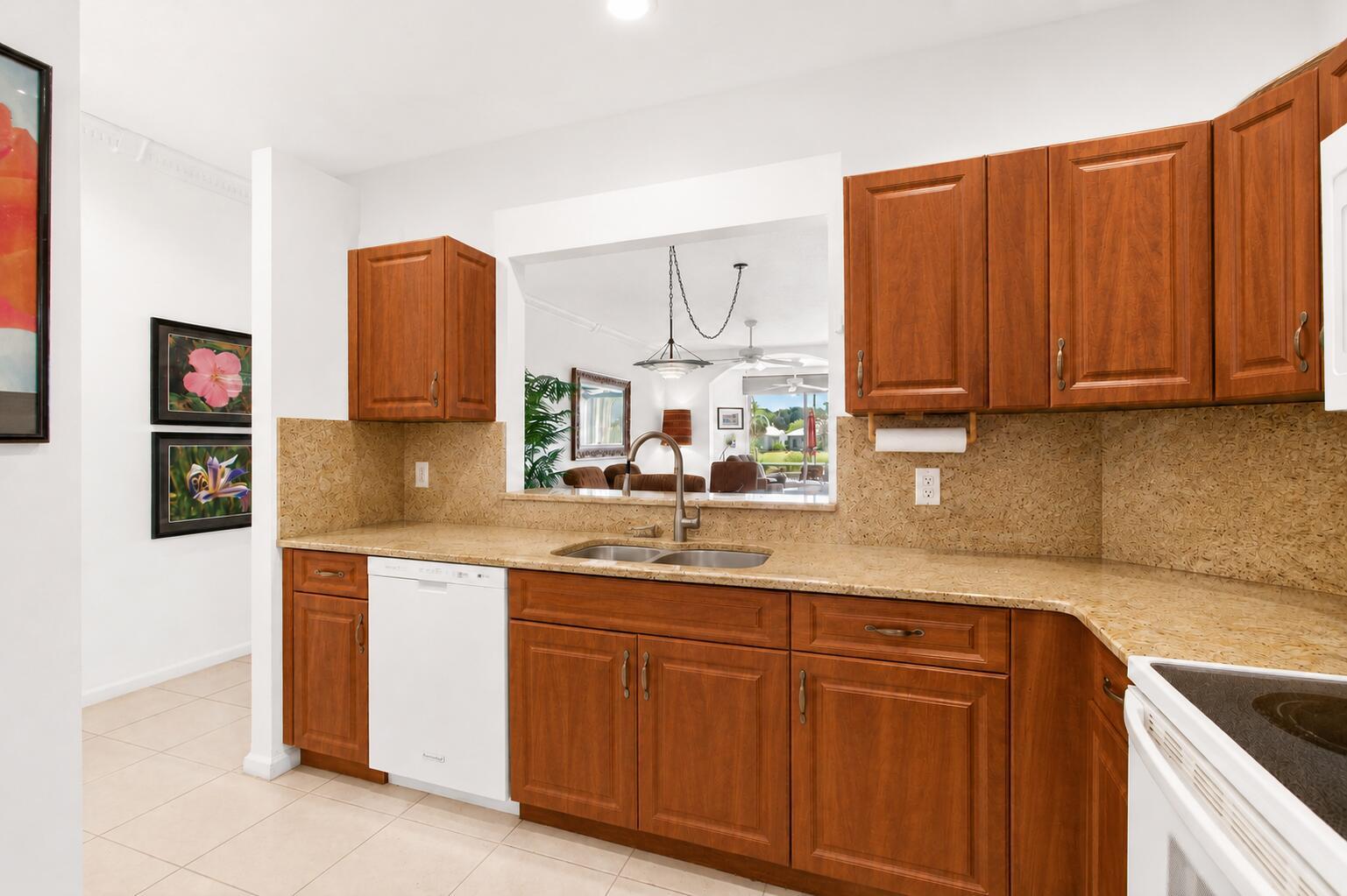 A kitchen features wood cabinets, granite countertops, a double sink, and a pass-through window — 10773 Royal Caribbean Circle, Boynton Beach FL 33437, BOYNTON BEACH, FL