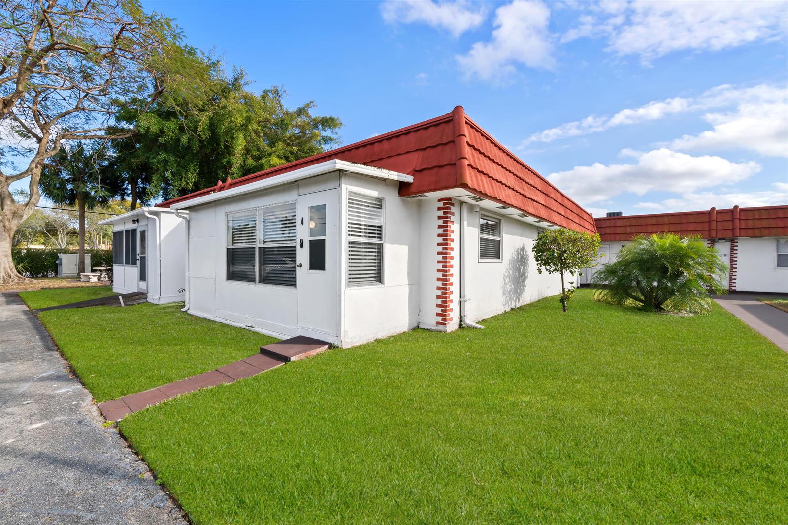 A white single-story building with a red metal roof sits on a grassy lawn — 4 Seville Terrace # 4, Delray Beach FL 33446, DELRAY BEACH, FL