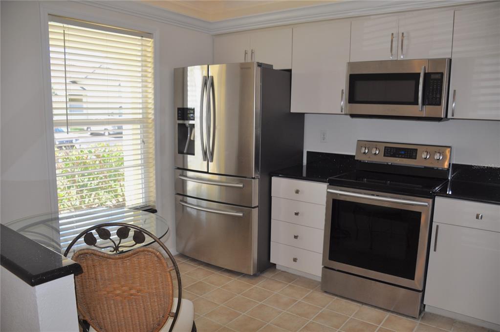 A kitchen features white cabinets, stainless steel appliances, black countertops, and a small dining area — 4000 BAL HARBOR BOULEVARD UNIT 214, PUNTA GORDA, FL