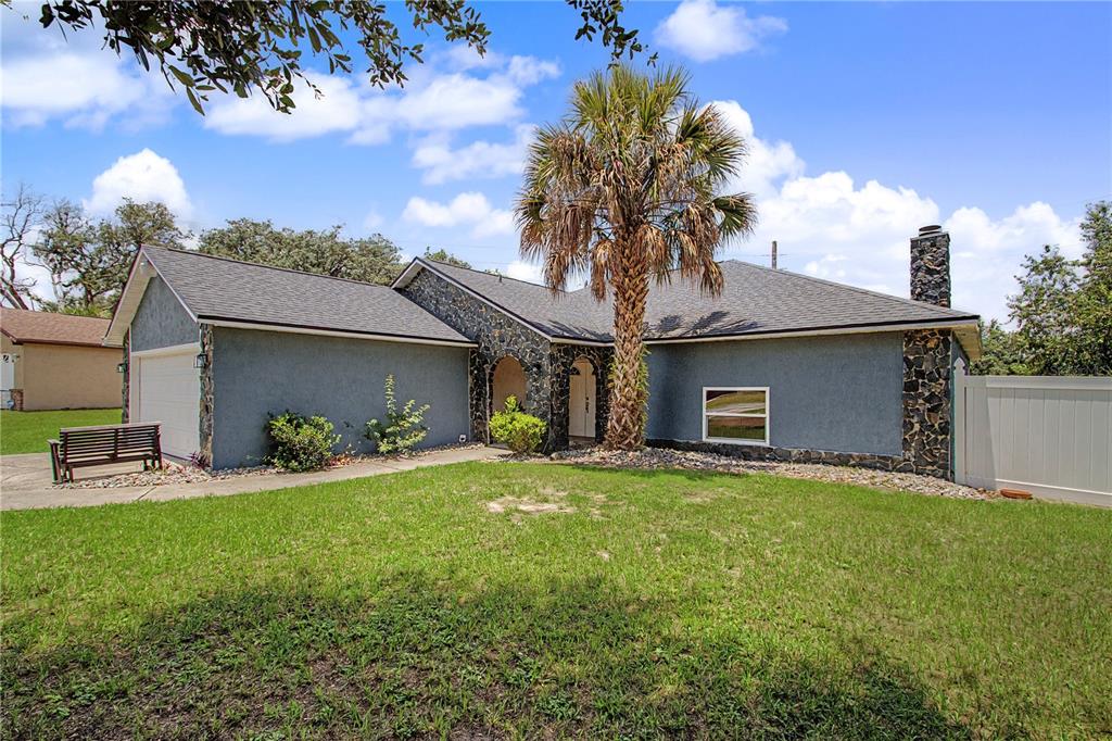 A single-story house with gray stucco walls, stone accents, a palm tree, and a garage — 14390 SW 46TH COURT, OCALA, FL
