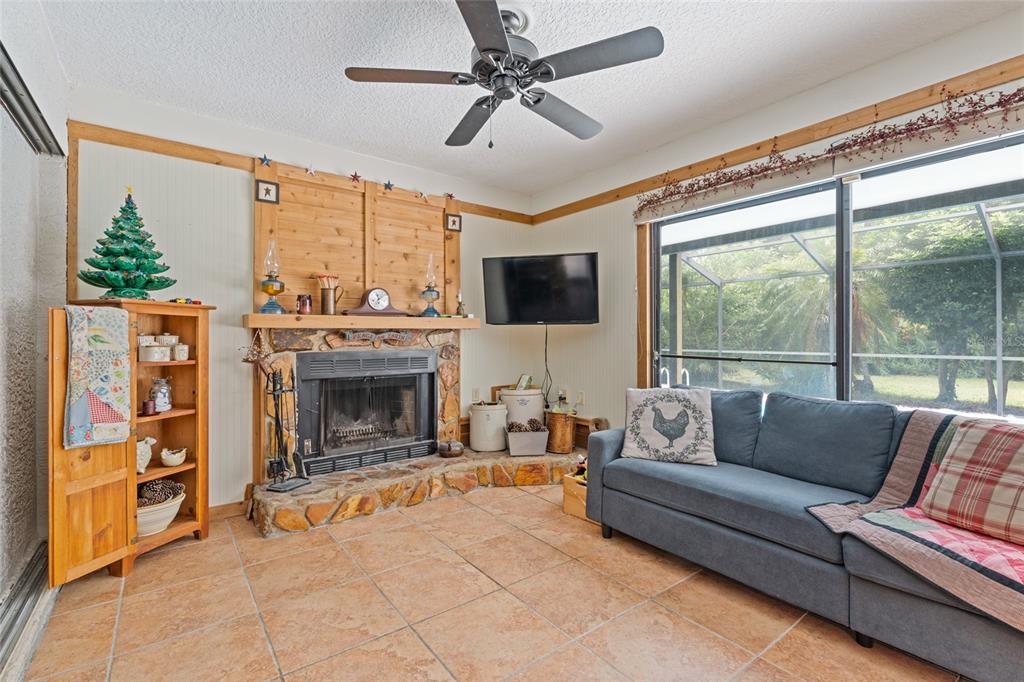 A living room features a stone fireplace, wood paneling, tile flooring, and a blue sofa — 155 WOODCUTTER LANE, PALM HARBOR, FL
