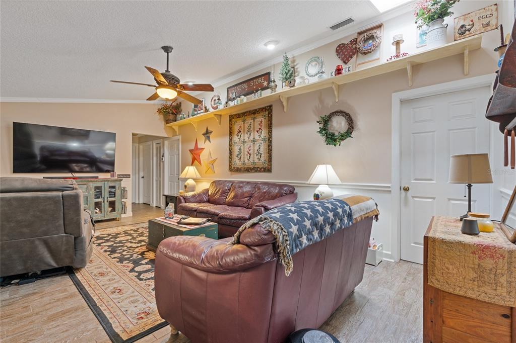 A living room features leather sofas, a ceiling fan, and a long wall-mounted display shelf — 155 WOODCUTTER LANE, PALM HARBOR, FL