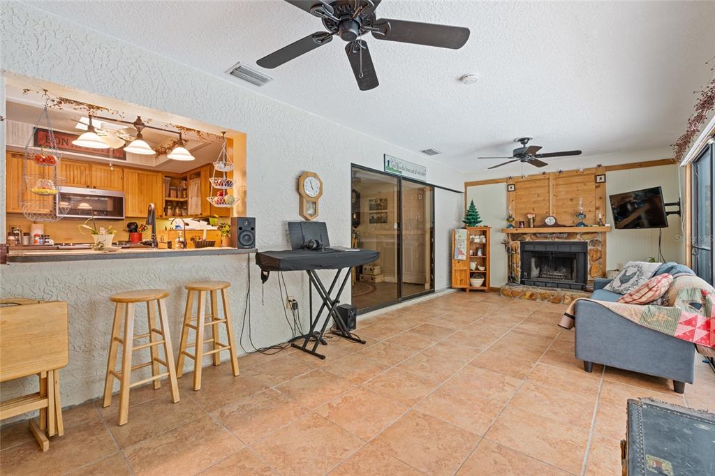 A living room with tile floors, a stone fireplace, and an open kitchen breakfast bar — 155 WOODCUTTER LANE, PALM HARBOR, FL