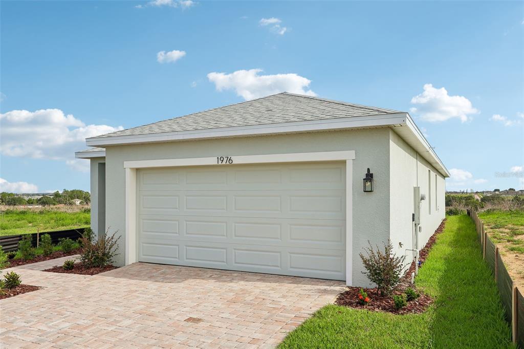 The exterior of a house features a light-colored garage door and a brick driveway — 1976 DIAMOND HEAD CIRCLE, HAINES CITY, FL