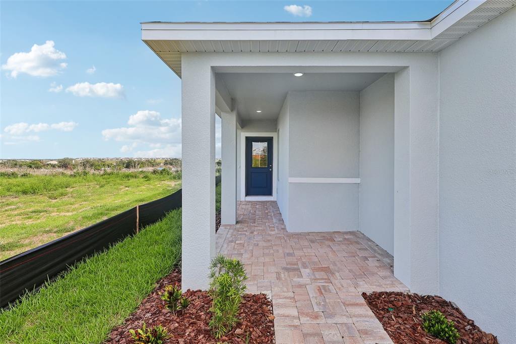 A covered entryway with a blue door and paver walkway overlooks an open grassy field — 1976 DIAMOND HEAD CIRCLE, HAINES CITY, FL