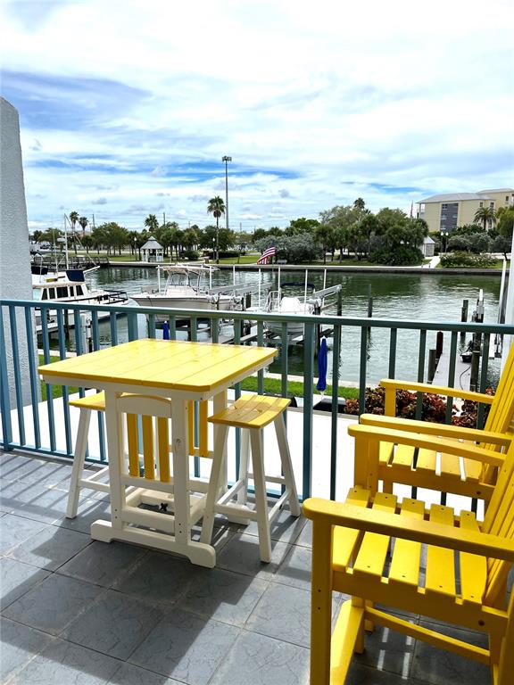 A yellow table and chairs sit on a balcony overlooking a canal with boats — 315 MEDALLION BOULEVARD UNIT H, MADEIRA BEACH, FL
