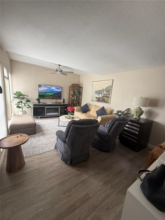 A living room features light wood-look flooring, a beige sofa, two gray recliners, and a television — 315 MEDALLION BOULEVARD UNIT H, MADEIRA BEACH, FL