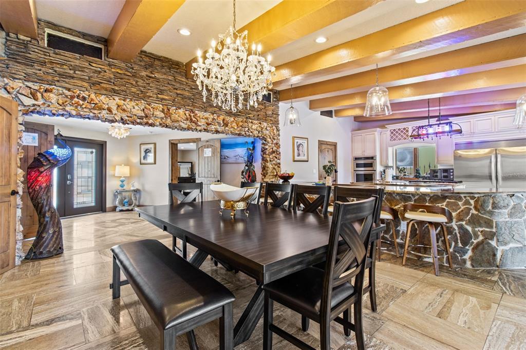 A dining area with a stone wall, wooden ceiling beams, and a crystal chandelier — 357 LA HACIENDA DRIVE, INDIAN ROCKS BEACH, FL
