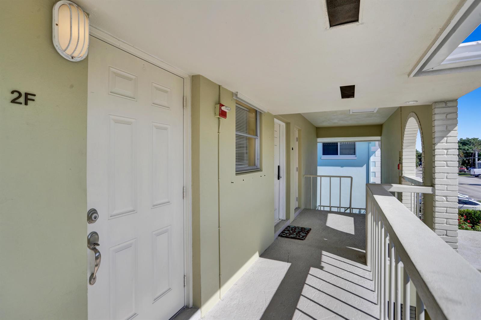 An outdoor apartment building walkway features a white door labeled 2F and a metal railing — 2311 NE 36th Street # 2f, Lighthouse Point FL 33064, LIGHTHOUSE POINT, FL
