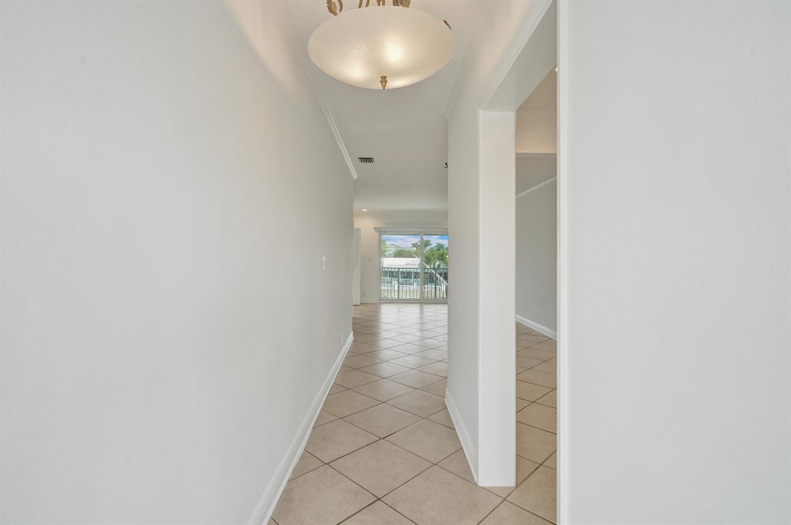A hallway with beige tile flooring leads toward a living area with sliding glass doors — 2311 NE 36th Street # 2f, Lighthouse Point FL 33064, LIGHTHOUSE POINT, FL