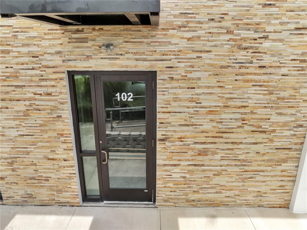 A glass door labeled 102 is set into a wall of stacked stone veneer — 3370 ROUSE ROAD UNIT 102, ORLANDO, FL