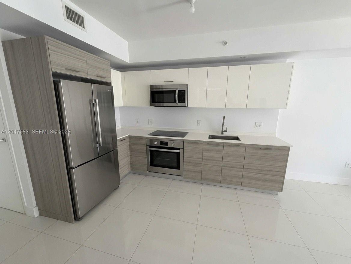 A modern kitchen features stainless steel appliances, light wood-grain lower cabinets, and white upper cabinets — 1300 Brickell Bay Dr # 1110, Miami FL 33131, MIAMI, FL