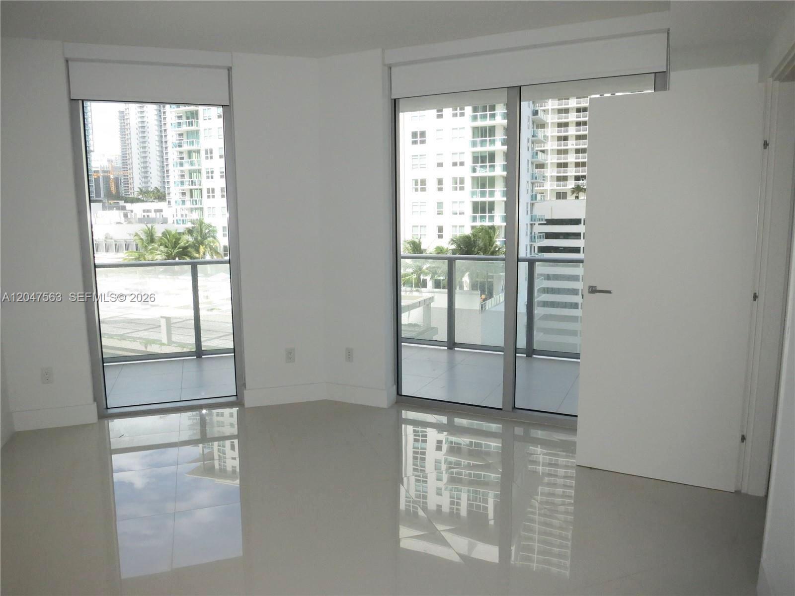 A bright, empty room features white tile floors, two glass balcony doors, and city views — 1300 Brickell Bay Dr # 1110, Miami FL 33131, MIAMI, FL