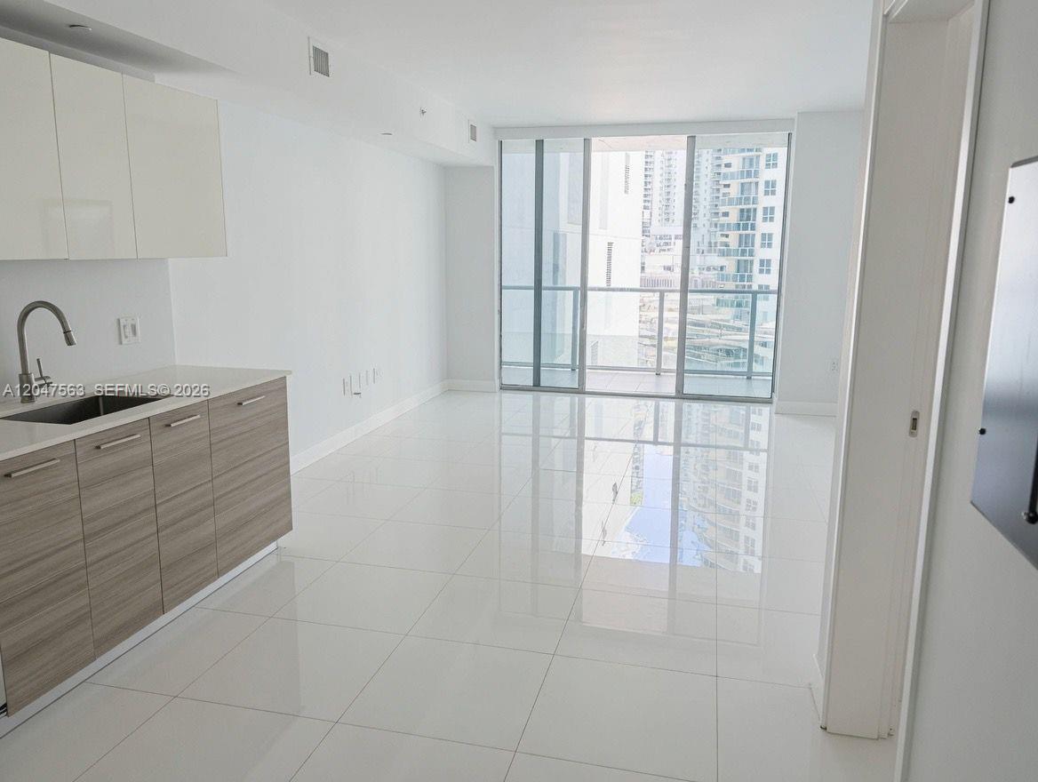 A modern kitchen with wood-toned cabinets opens into a bright living area with floor-to-ceiling windows — 1300 Brickell Bay Dr # 1110, Miami FL 33131, MIAMI, FL