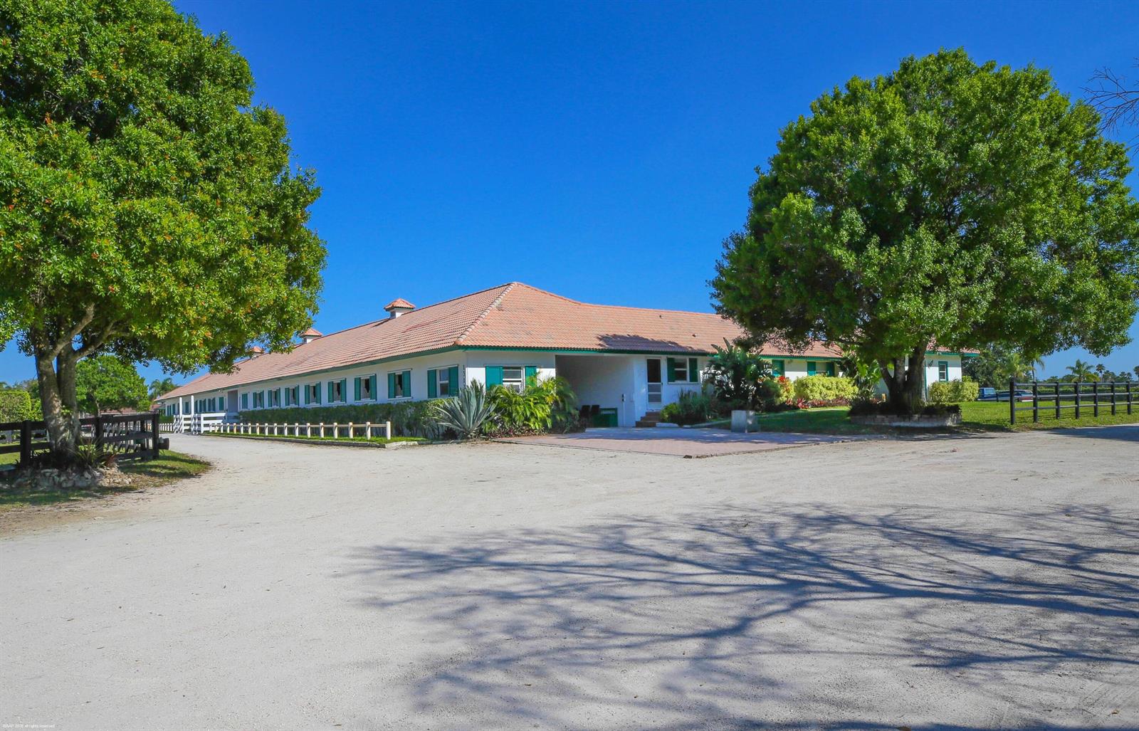 A long, single-story white horse stable with a terracotta tile roof and green shutters — 13122 52nd Place S, Wellington FL 33449, WELLINGTON, FL