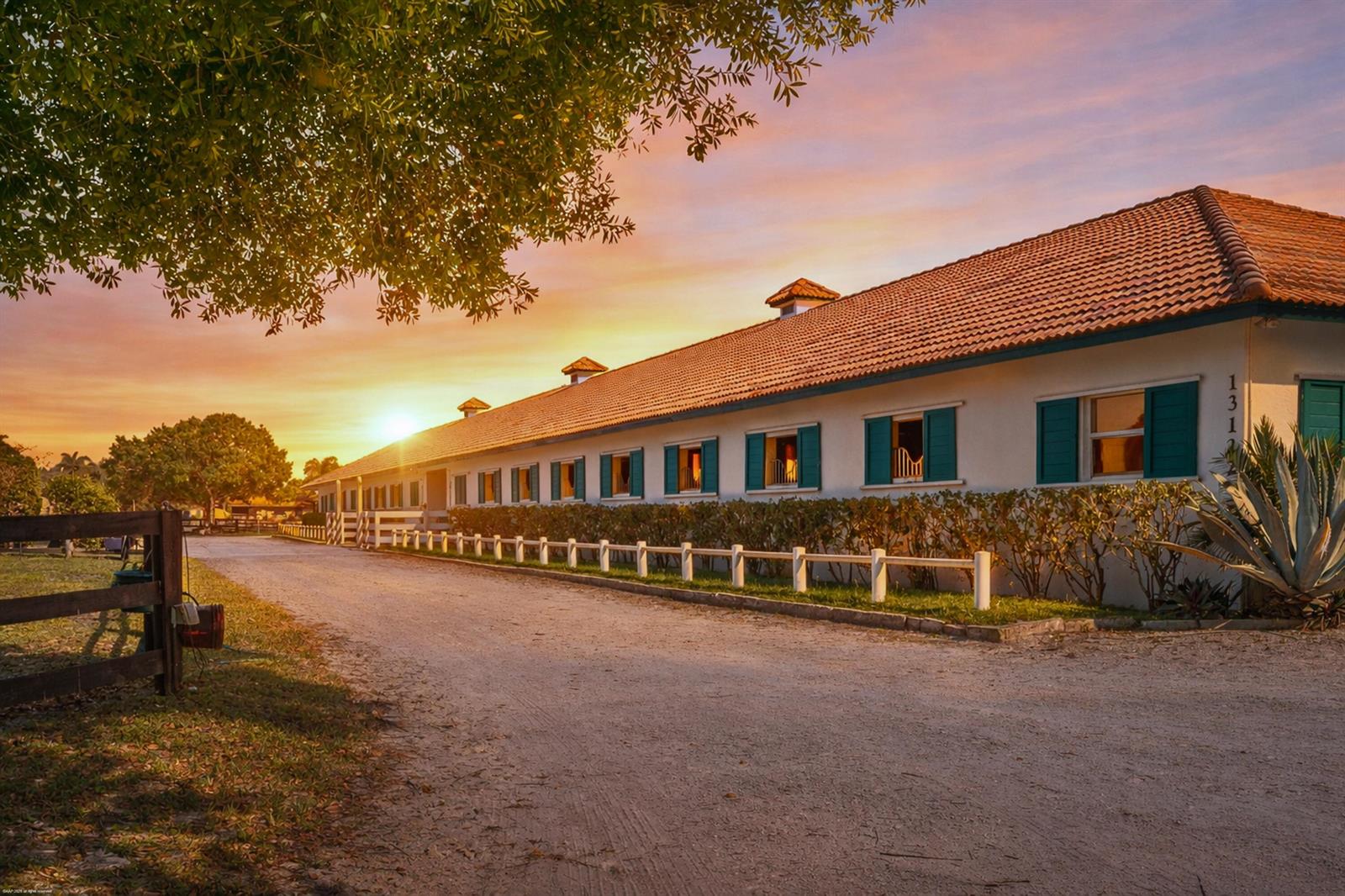 A long, white horse stable with a tiled roof and teal shutters at sunset — 13122 52nd Place S, Wellington FL 33449, WELLINGTON, FL
