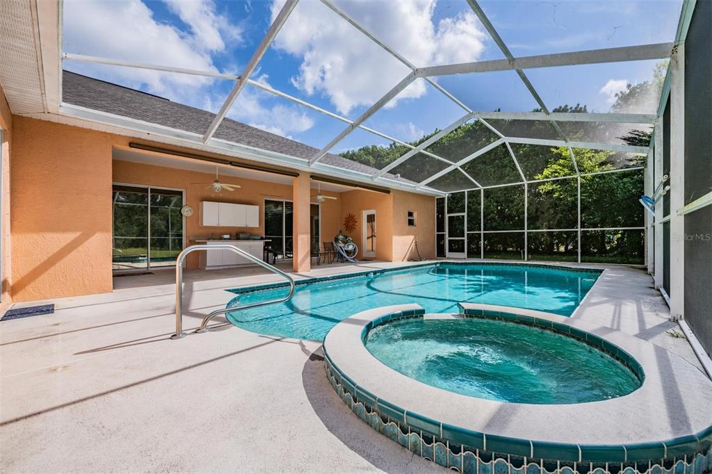 A screened-in patio features a swimming pool, a raised hot tub, and a covered area — 13566 RUDI LOOP, SPRING HILL, FL