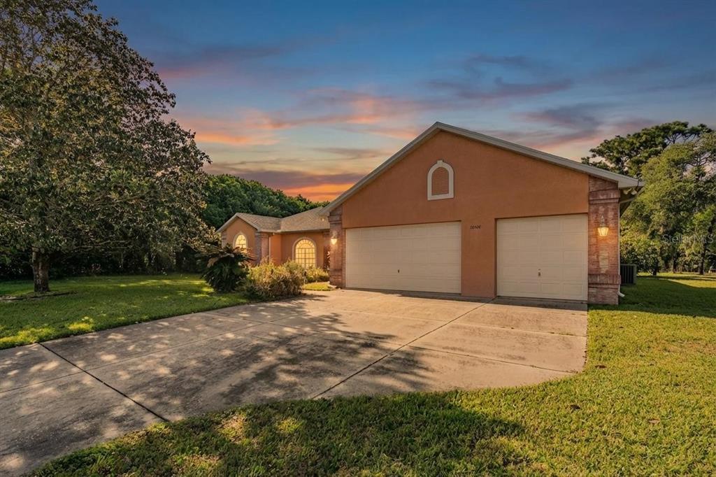 A single-story house with a two-car garage and a concrete driveway at sunset — 13566 RUDI LOOP, SPRING HILL, FL