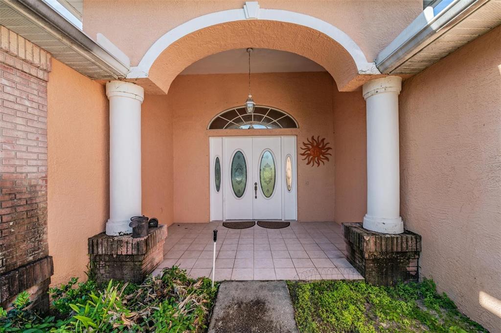 A covered front porch features white double doors with glass inserts and two large columns — 13566 RUDI LOOP, SPRING HILL, FL