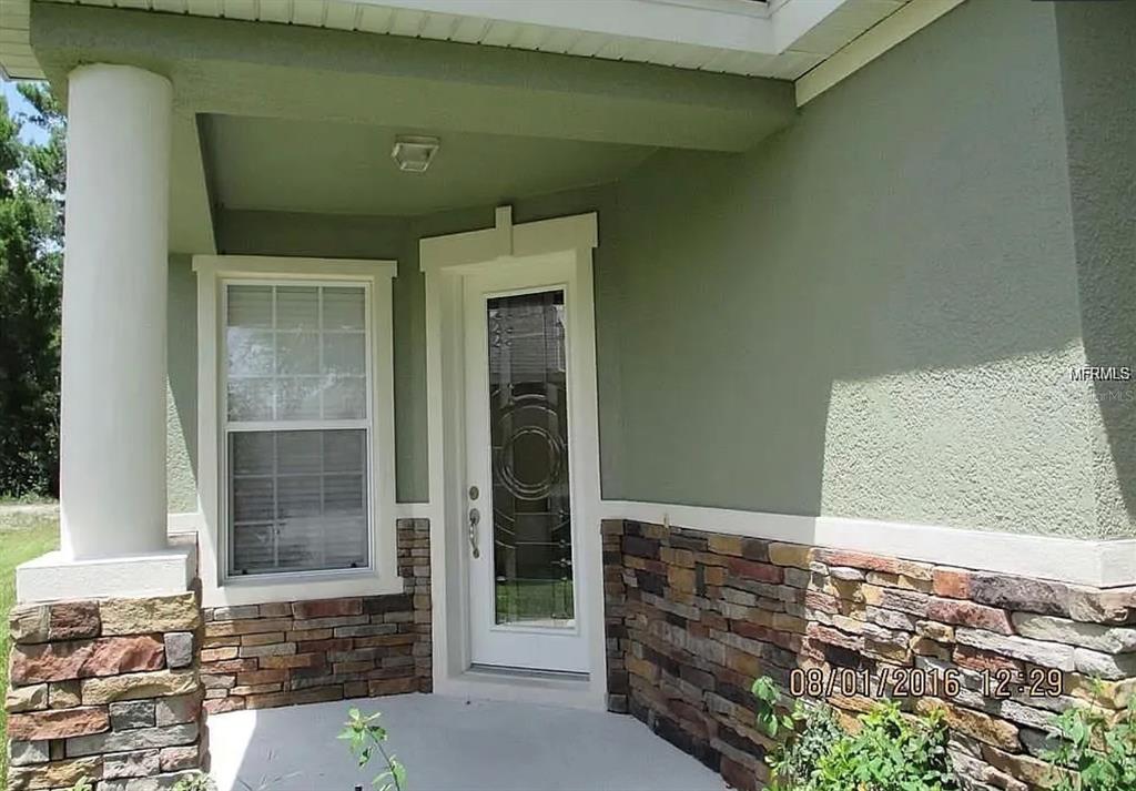 A covered entryway features a white front door, a window, and stone veneer siding — 3260 SORREL COURT, DELTONA, FL