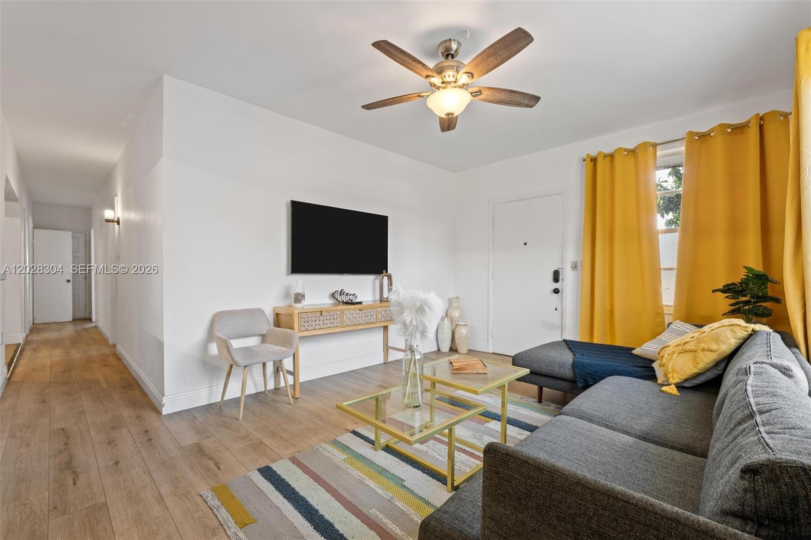 A living room features a gray sofa, glass coffee tables, a wall-mounted television, and yellow curtains — 2453 SW 17th St, Miami FL 33145, MIAMI, FL