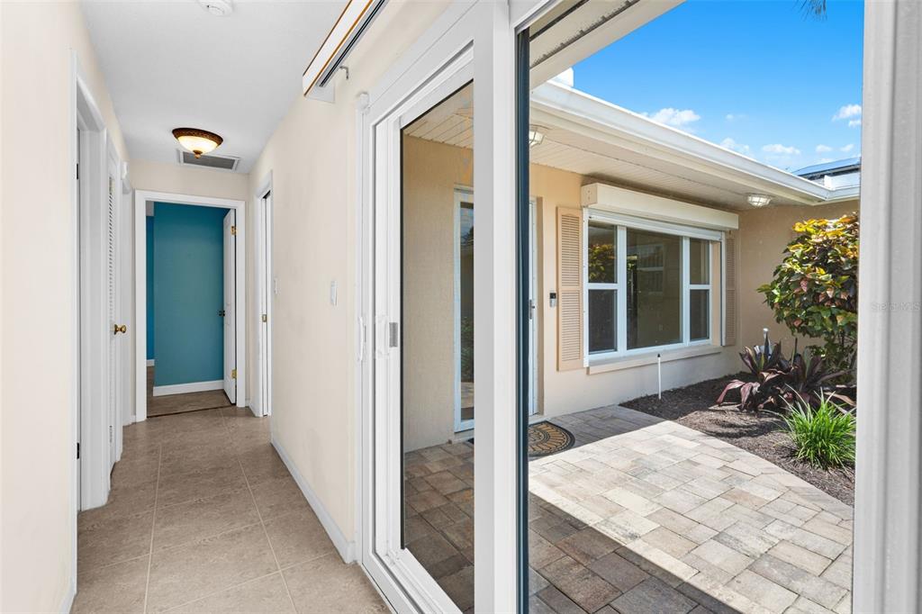 A tiled hallway leads to a doorway, with sliding glass doors opening to a paved courtyard — 27 WESTVIEW LANE, COCOA BEACH, FL