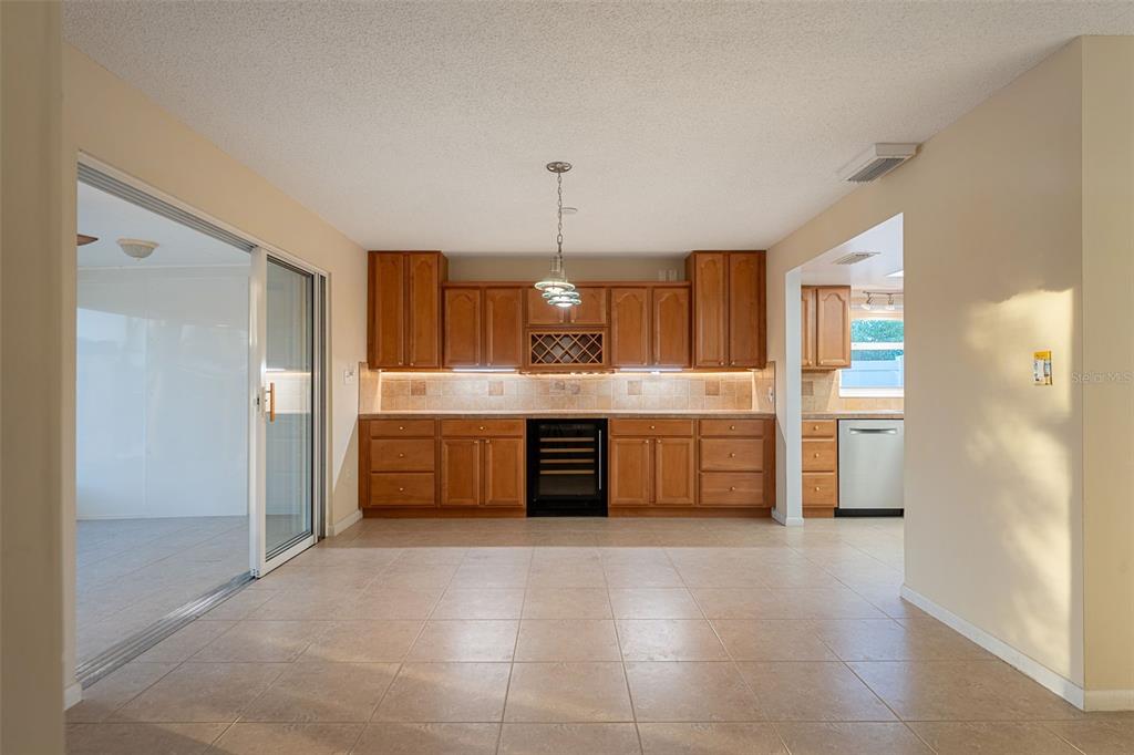 A kitchen featuring wood cabinets, a wine cooler, and tile flooring, with an adjacent sliding door — 27 WESTVIEW LANE, COCOA BEACH, FL